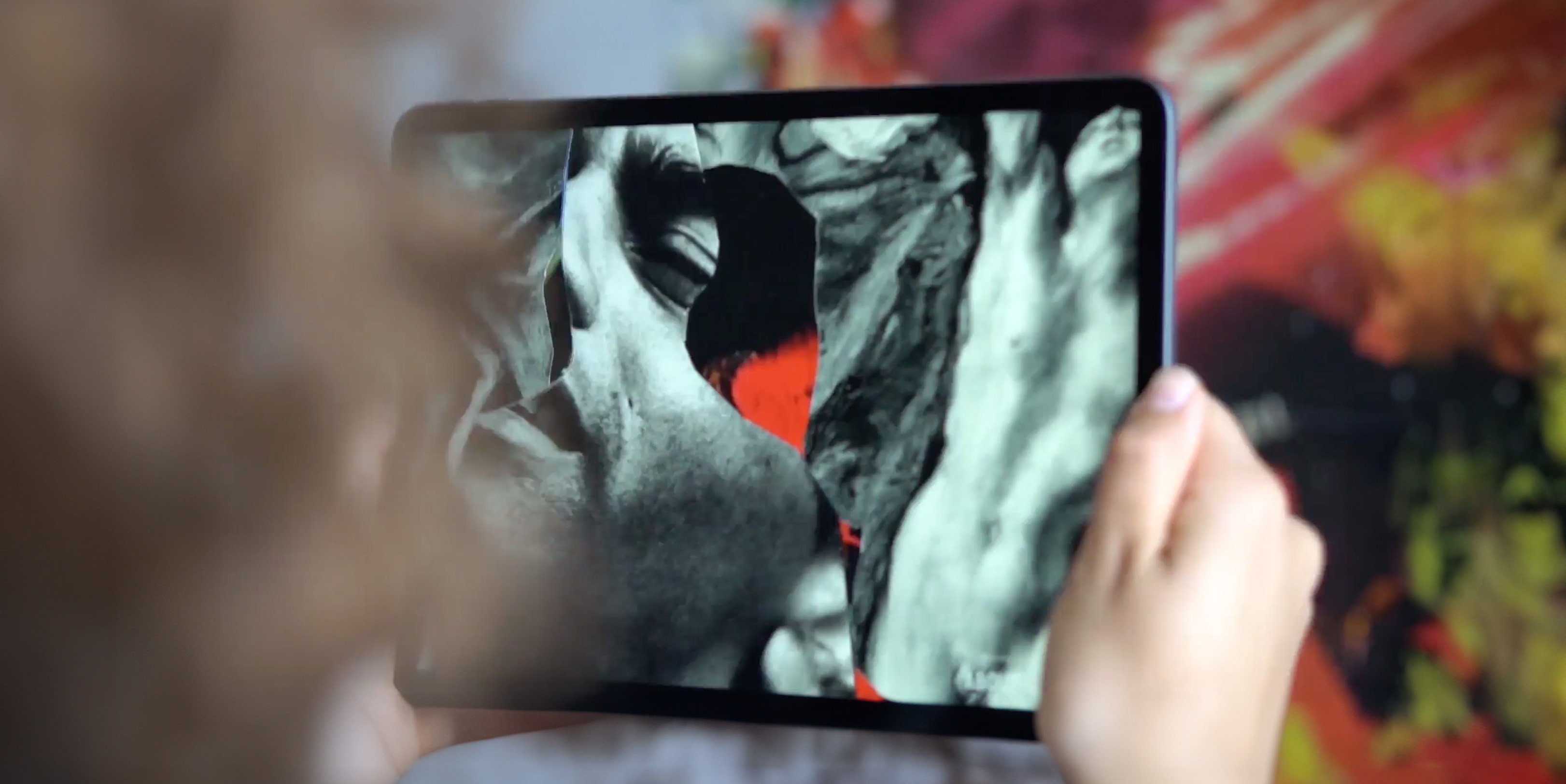 A person holds a tablet displaying a vibrant, digitally enhanced image of a figure with dynamic lighting effects.