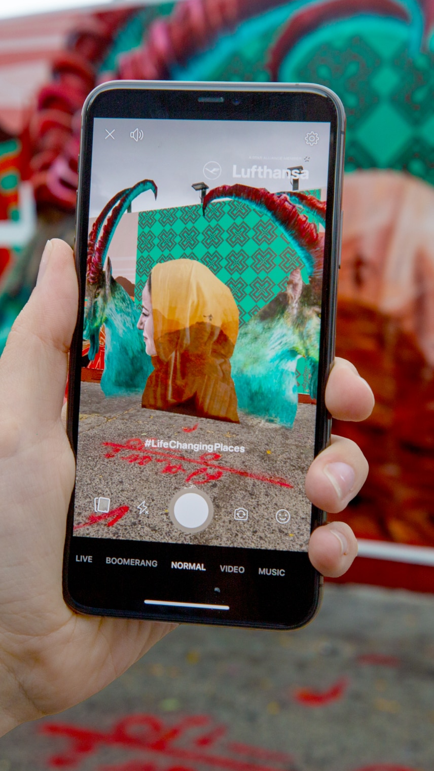 Eine Hand hält ein Handy, das AR Effekte vor farbenfrohen Kunstwerken zeigt.