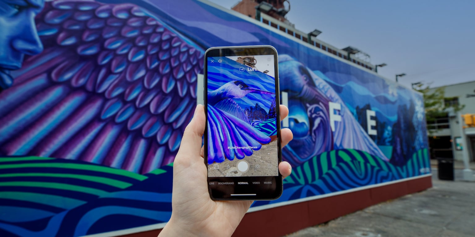 Eine Person macht mit ihrem Smartphone ein Foto von einem lebhaften AR Mural mit bunten Flügeln und einem Vogel.