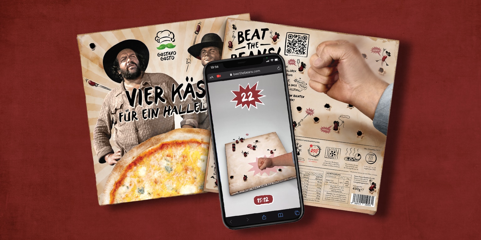 A smartphone displays a game interface while two playful characters promote a cheesy pizza package titled "Vier Käse für ein Halleluja.