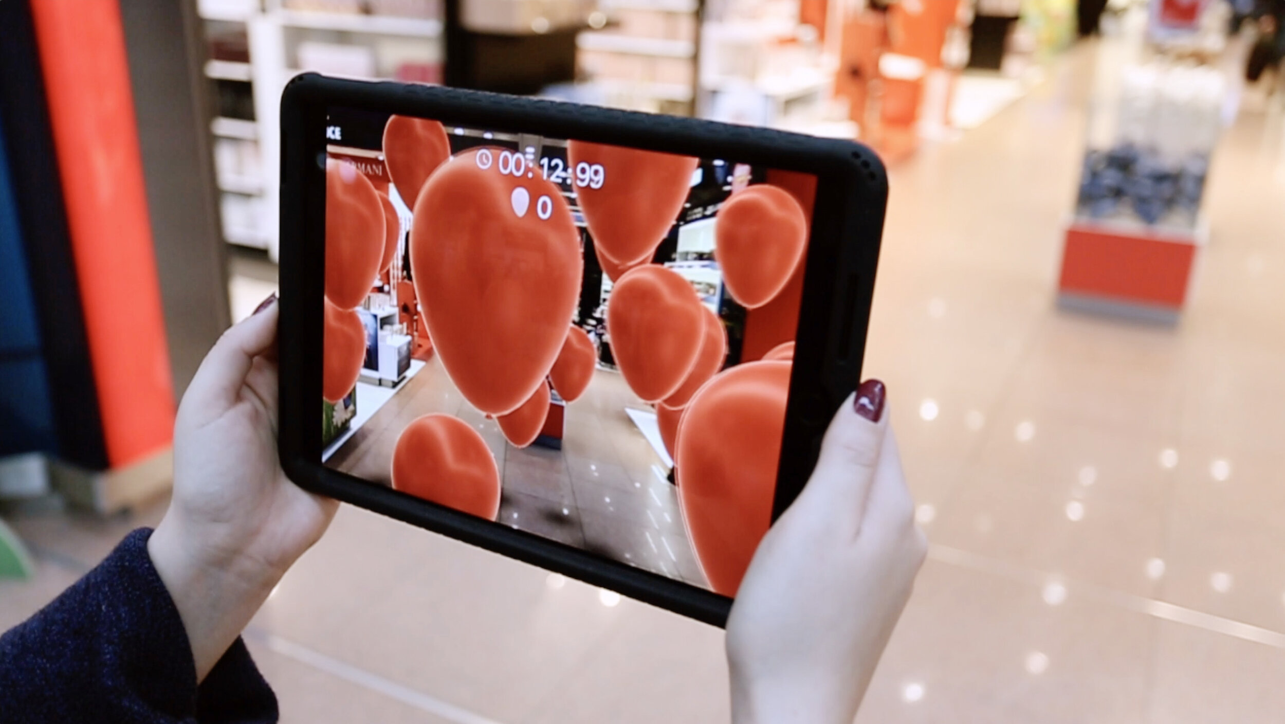 A person is using a tablet to view an augmented reality scene filled with floating red hearts in a shopping mall. 