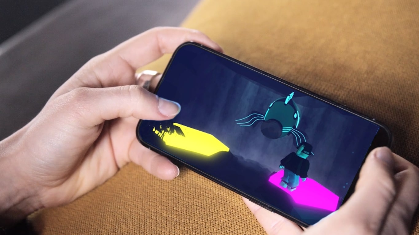 A person's hands are seen holding a phone displaying a colorful video game character on the screen.