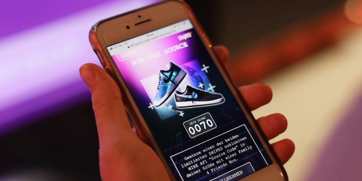 A person holds a smartphone displaying a contest for limited edition sneakers with a score of 070.