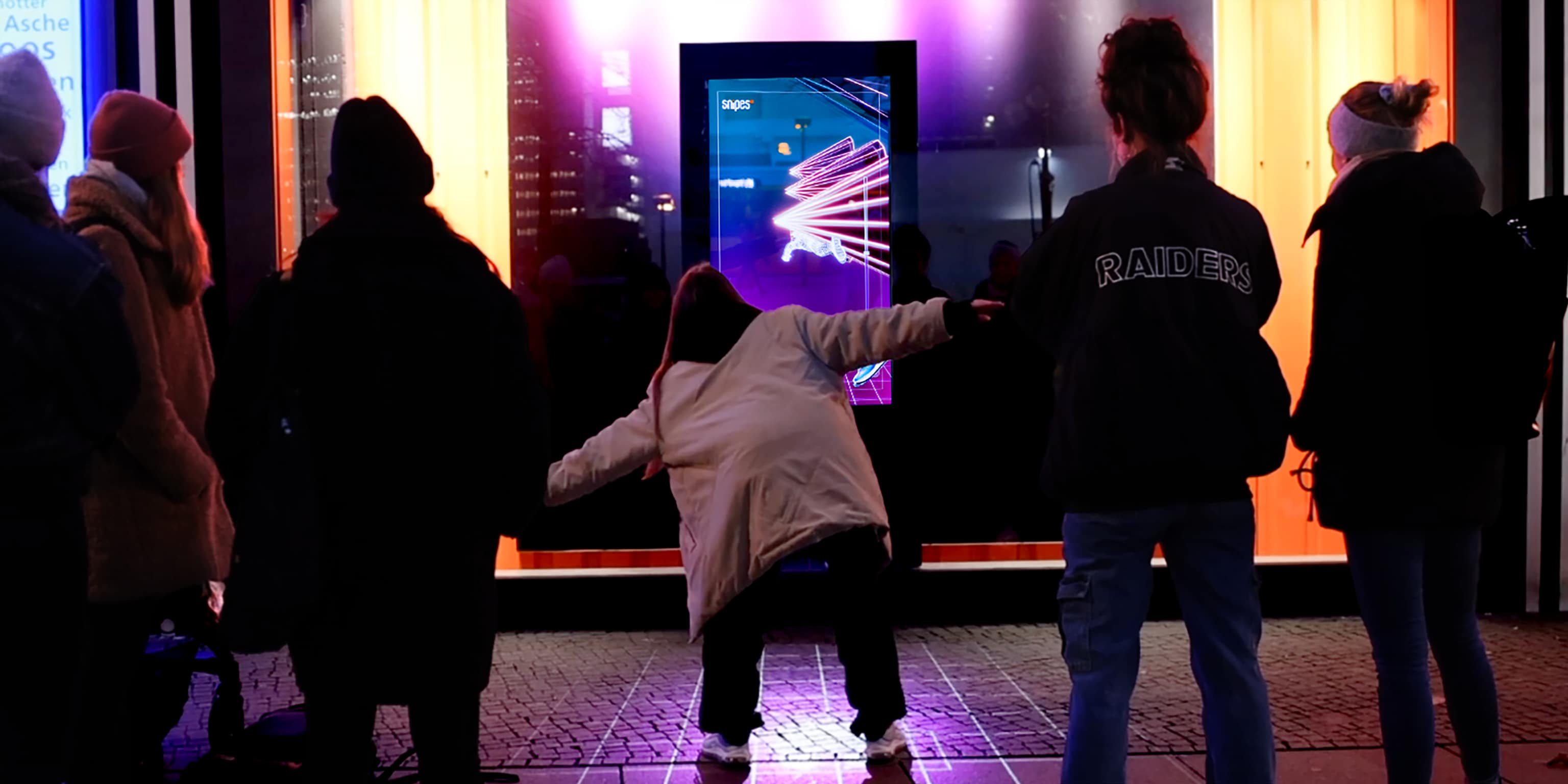 A group of people playfully interacts with a colorful illuminated display in a Snipes Storefront.
