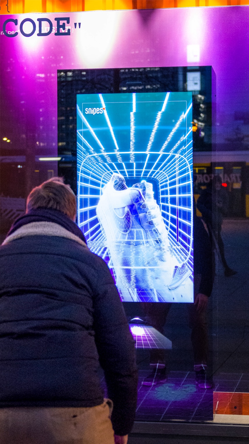 A person stands in front of a digital display featuring a striking 3D representation of shoes against a vibrant, illuminated background.