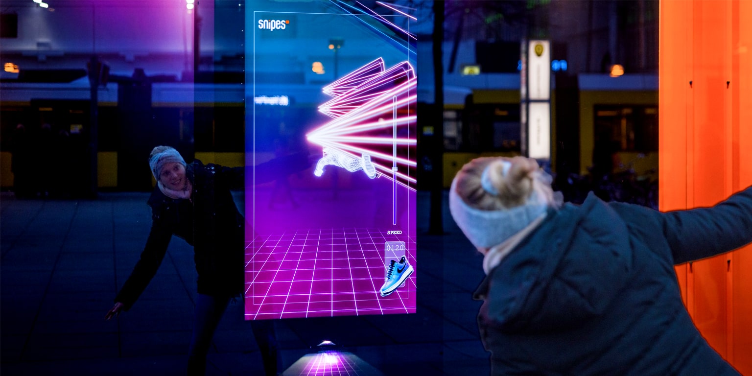 A woman interacts playfully with a digital display showcasing a futuristic sneaker design in vibrant colors.