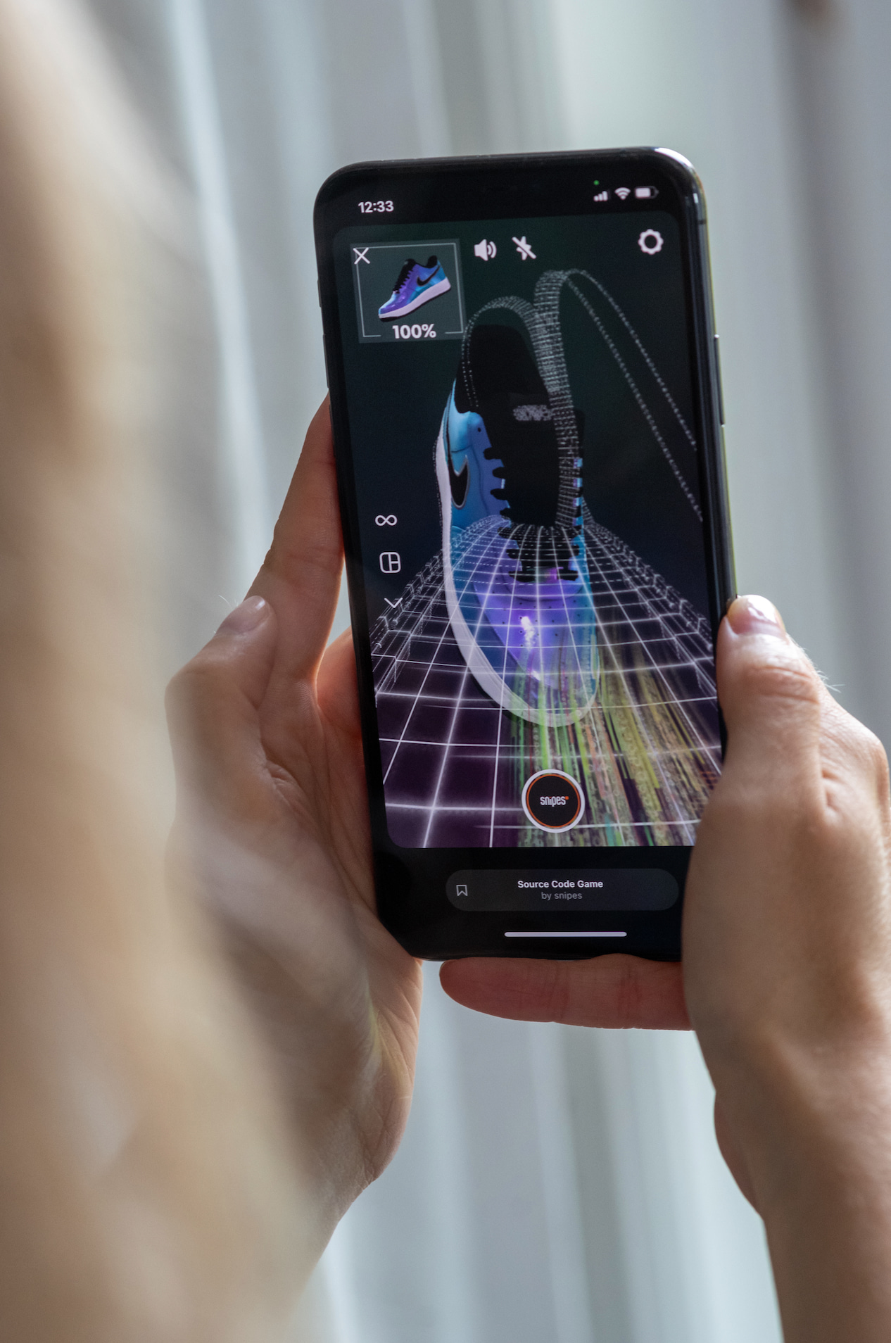 A person is holding a smartphone displaying an augmented reality filter for Snipes with a sneaker over a digital grid background.