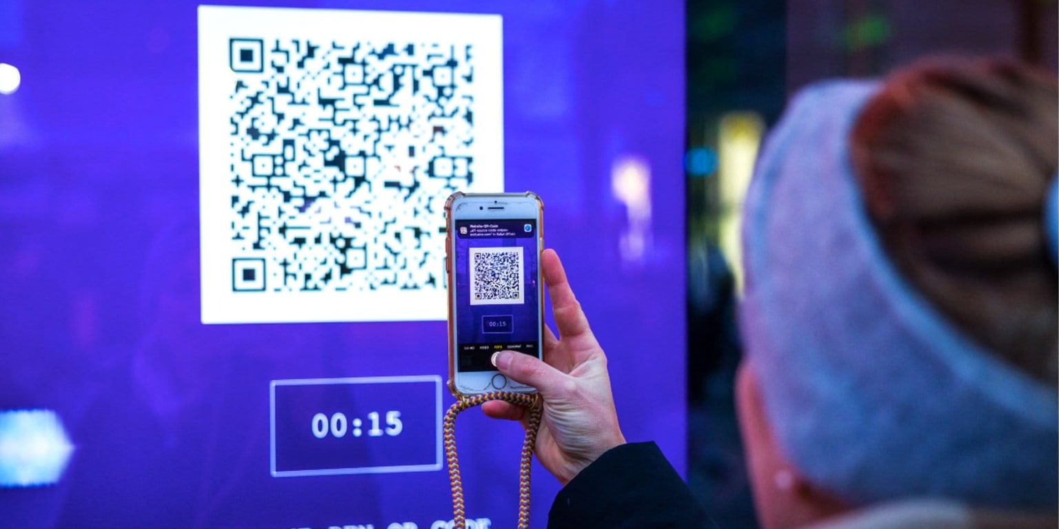A person scans a QR code displayed on a large screen.