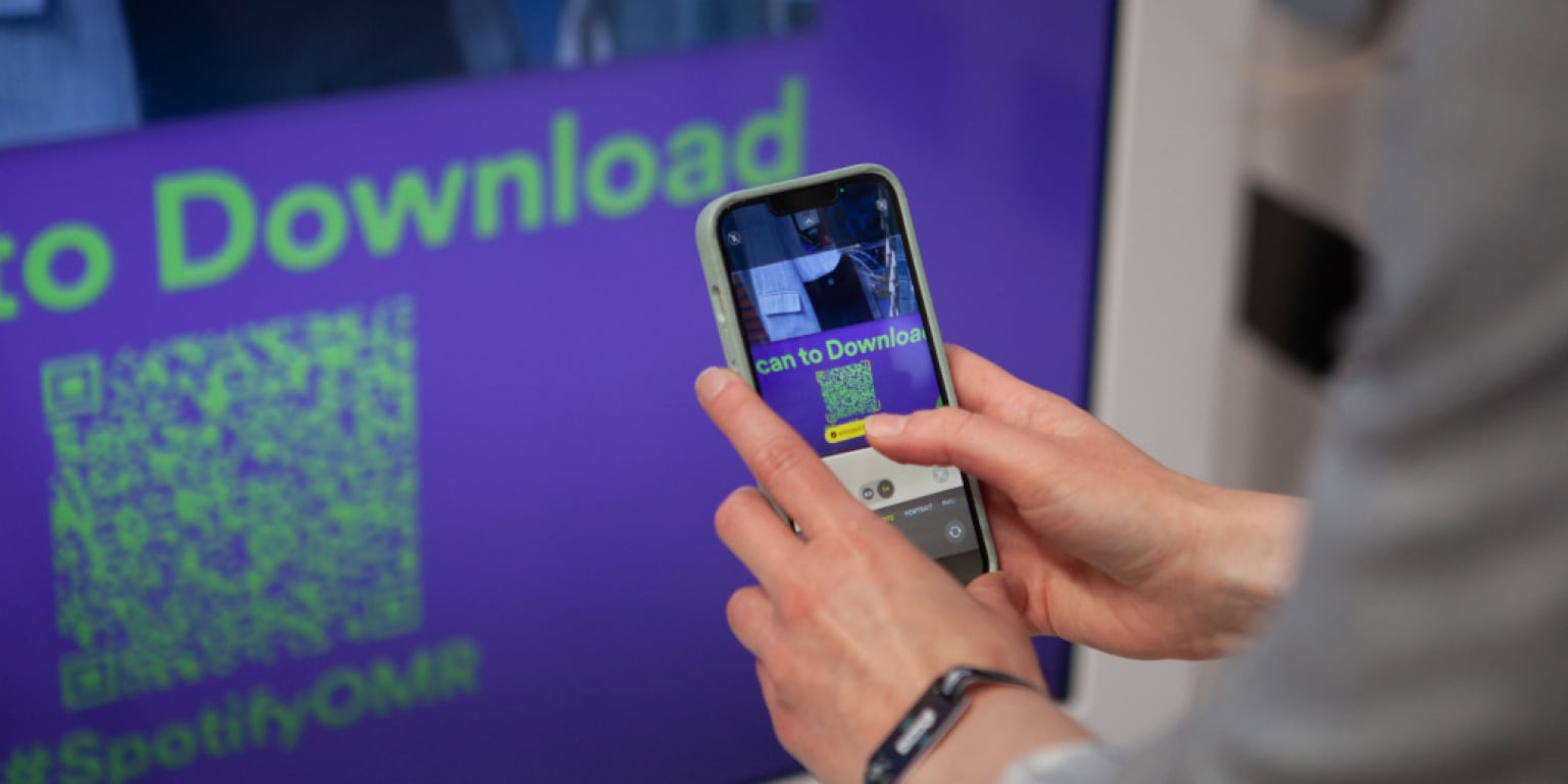 A person scans a QR code on a screen using their smartphone to download an application.