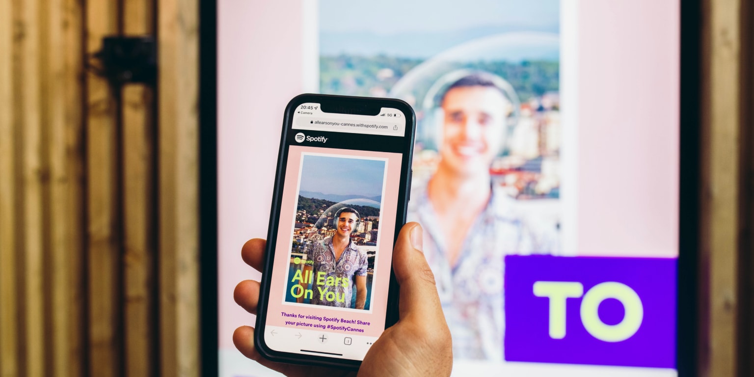 A smartphone displays a Spotify poster featuring a smiling person with a scenic background.